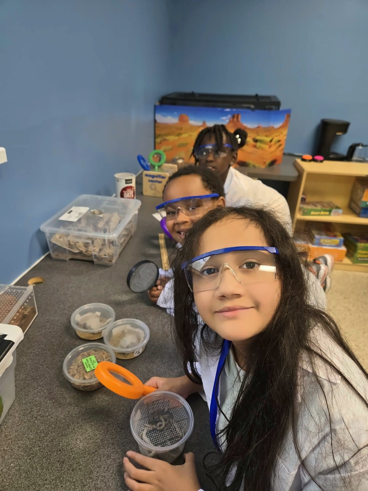 A smiling SWREA student in safety goggles at the science table