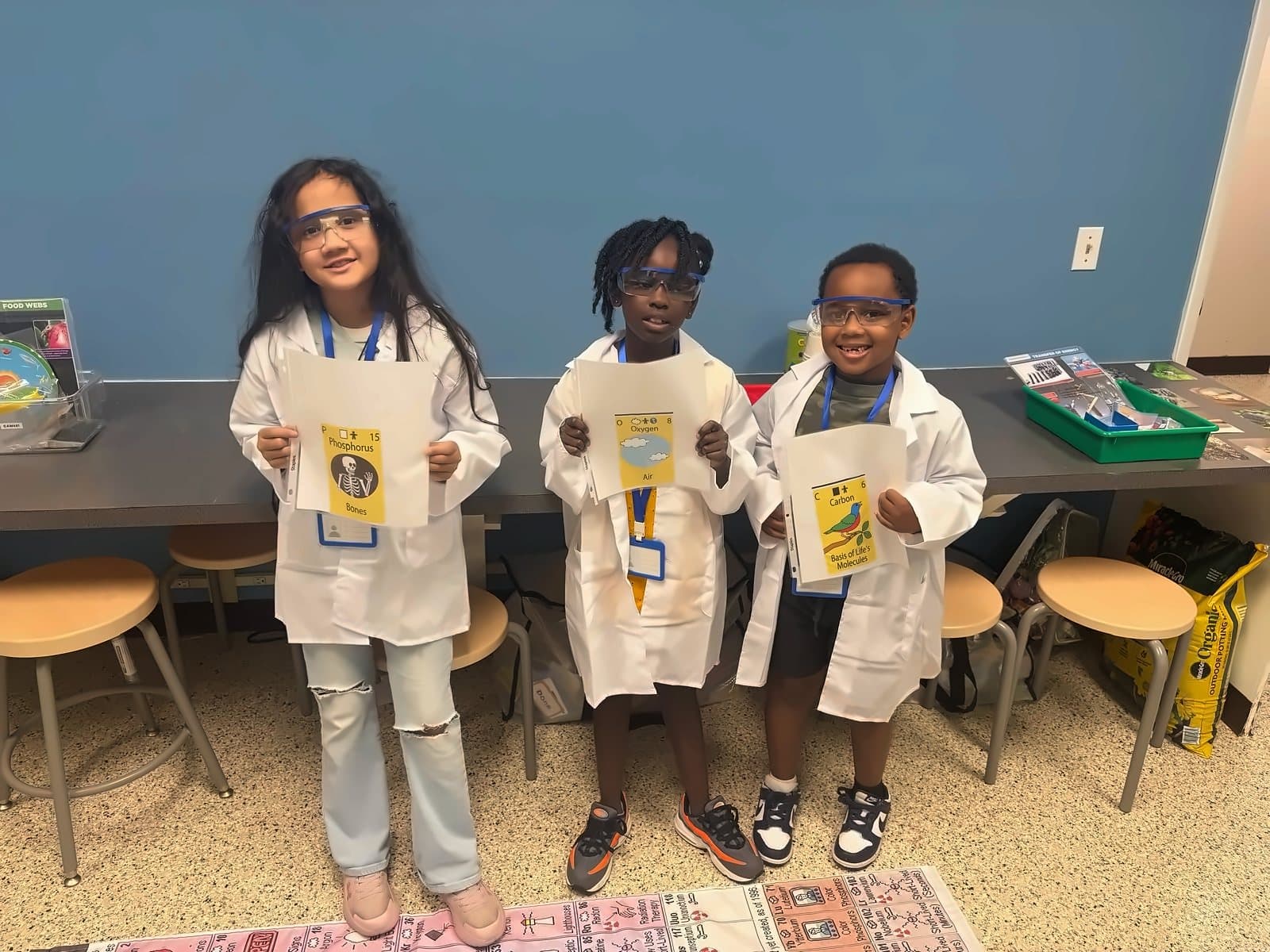 Three SWREA students in lab coats holding their science badges