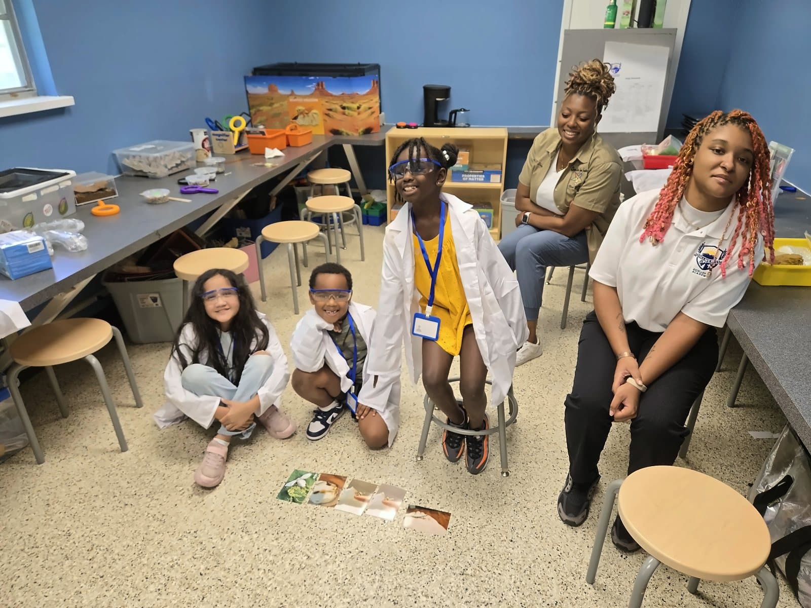 SWREA students in lab coats sitting in a circle with Ms. Jayla and staff