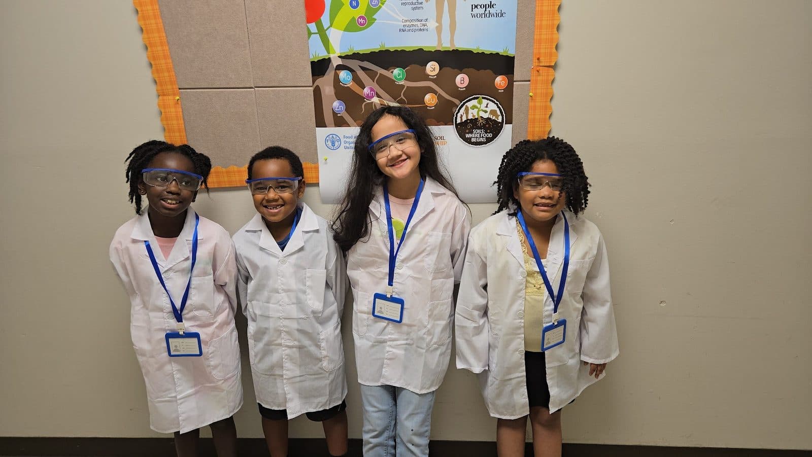 Cuatro estudiantes de Still We Rise Excellence Academy con batas de laboratorio y gafas de seguridad durante una clase de ciencias